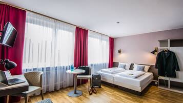 Habitación de hotel con cama, escritorio con una computadora portátil, silla, mesa y televisión.