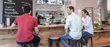 Una zona de bar con taburetes, un menú en una pizarra y estantes con botellas y copas.