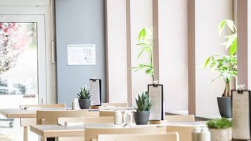 Un comedor moderno con mesas y sillas de madera, plantas en macetas e iluminación colgante.