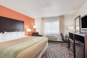 A hotel room with a large bed, a desk with a chair, a television, and a window with curtains. - Ramada By Wyndham Coeur D'alene (Coeur d'Alene)