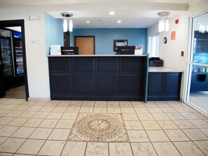 A reception area with a dark blue counter, a tiled floor with a decorative pattern, a clock, and a vending machine. - Ramada By Wyndham Coeur D'alene (Coeur d'Alene)