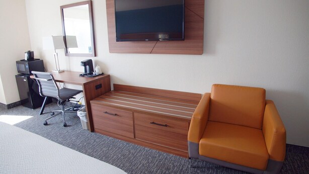 A hotel room with a bed, a desk with a computer and coffee maker, a TV mounted on the wall, and an orange chair. - Ramada By Wyndham Coeur D'alene (Coeur d'Alene)