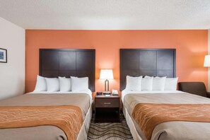 A hotel room with two beds, a nightstand with a lamp, and a patterned rug. - Ramada By Wyndham Coeur D'alene (Coeur d'Alene)