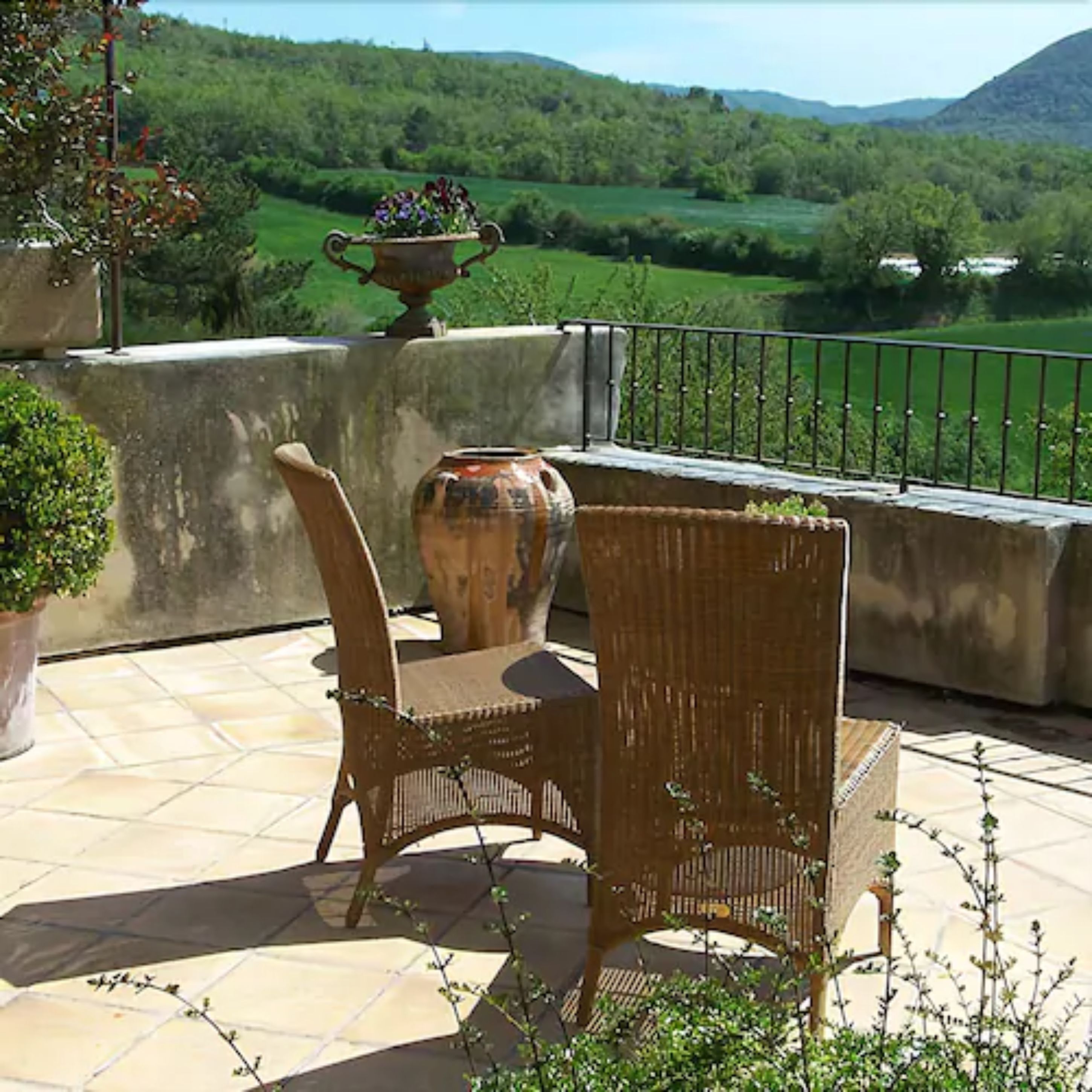 Un patio con una silla de mimbre, un jarrón grande y una planta en maceta.