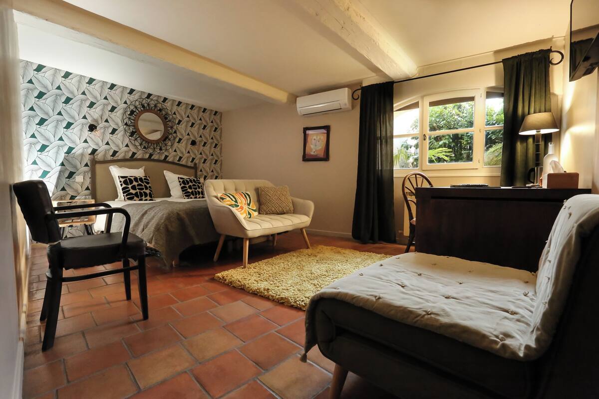 A cozy room with a bed, two chairs, a desk, and a window with curtains.