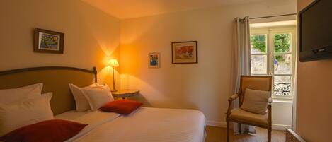A hotel room with a large bed, a chair, a TV, and a window with curtains.