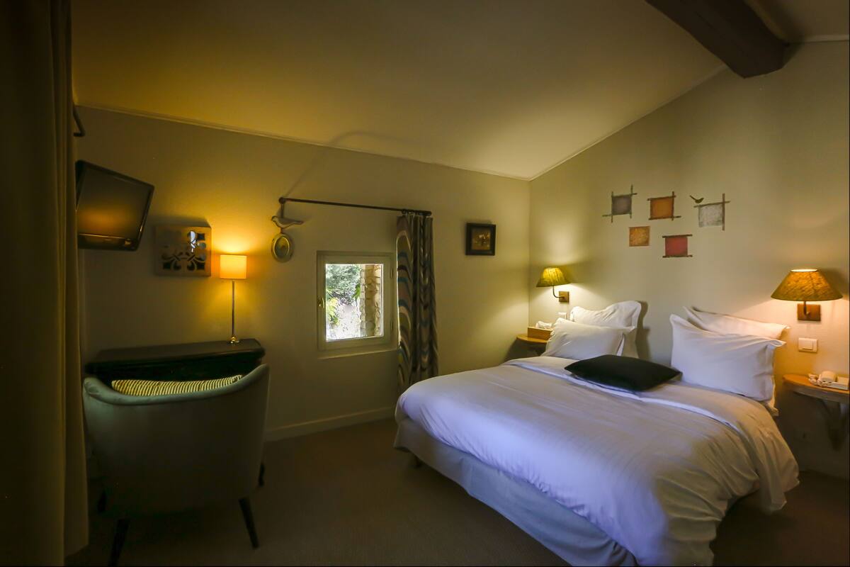 A bedroom with a bed, a chair, a desk, and a window.