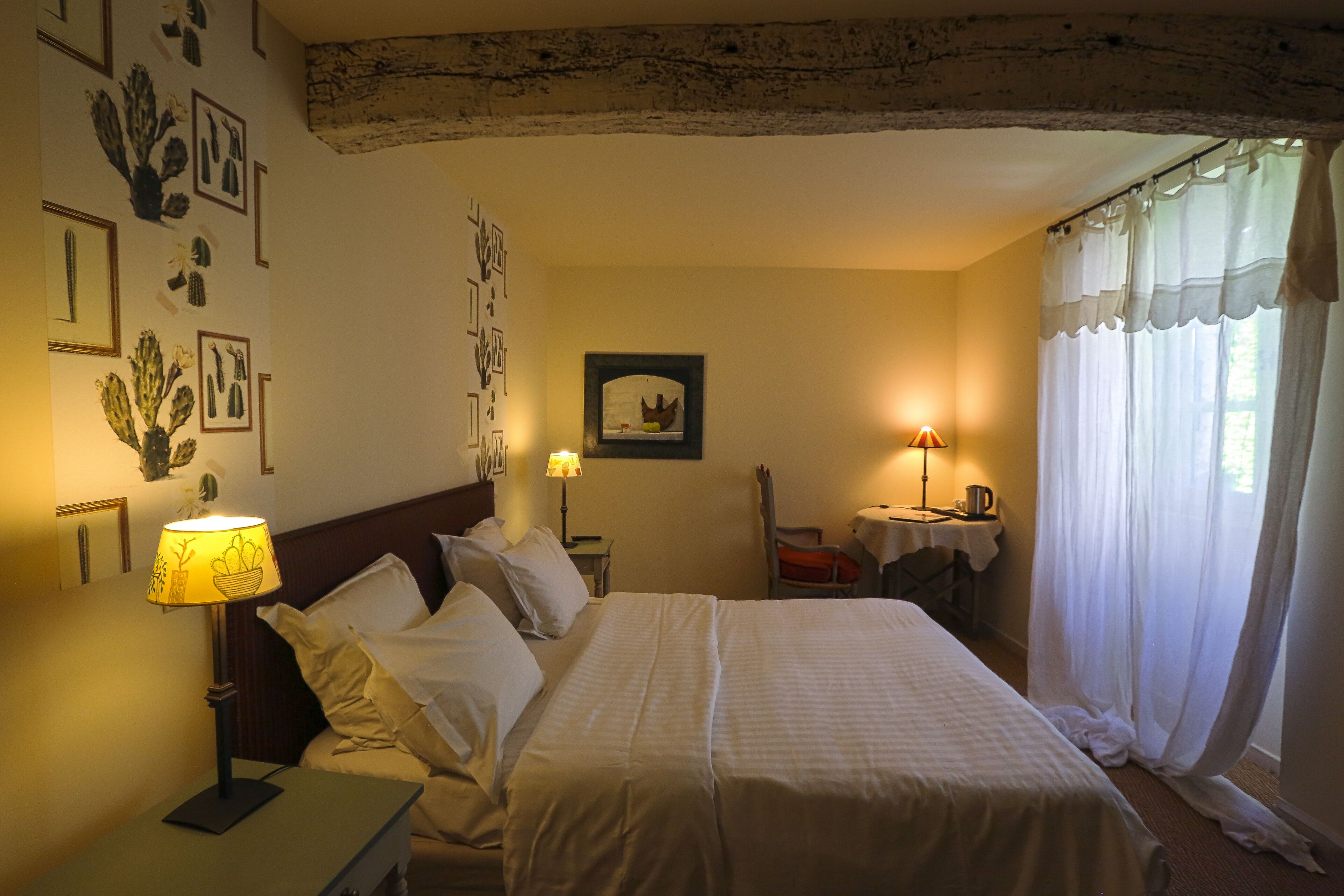 Camera d'albergo con un letto grande, due comodini, una scrivania con una sedia e una finestra con tende.