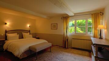 A bedroom with a bed, bedside table, lamp, window with curtains, radiator, and a picture on the wall.