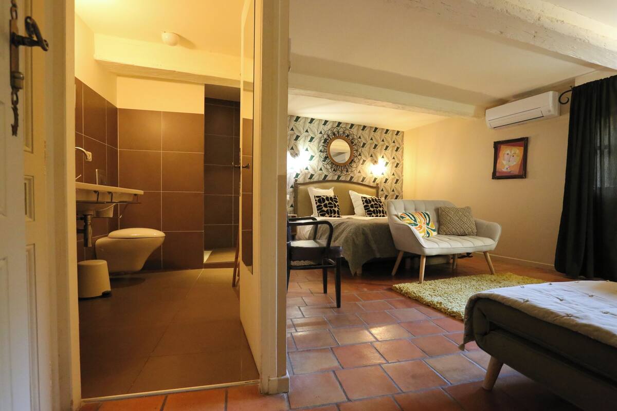 A hotel room with a bathroom, a bed, a sofa, and a small table.