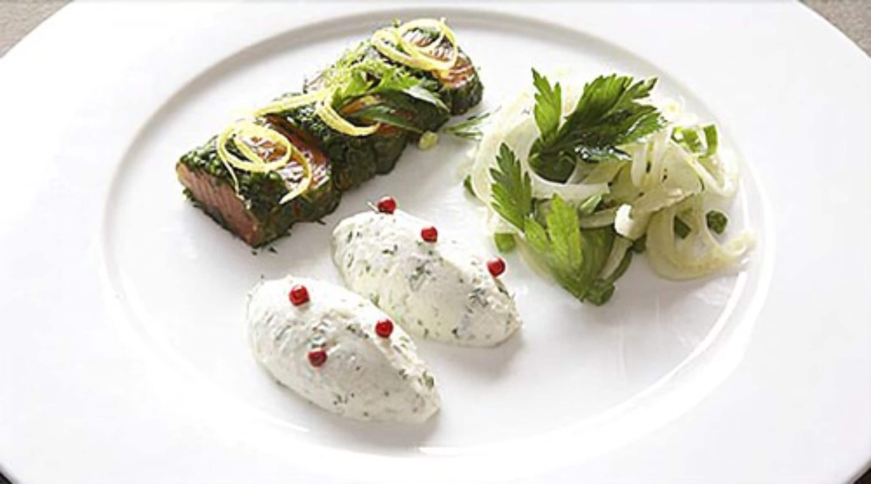 Une assiette contenant un morceau de viande, deux cuillerées d’une sauce crémeuse et une salade en accompagnement.
