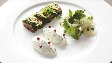 Une assiette contenant un morceau de viande, deux cuillerées d’une sauce crémeuse et une salade en accompagnement.