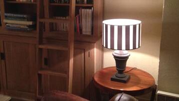 Une pièce avec une bibliothèque en bois remplie de livres, une table ronde en bois surmontée d’une lampe et un fauteuil en cuir.