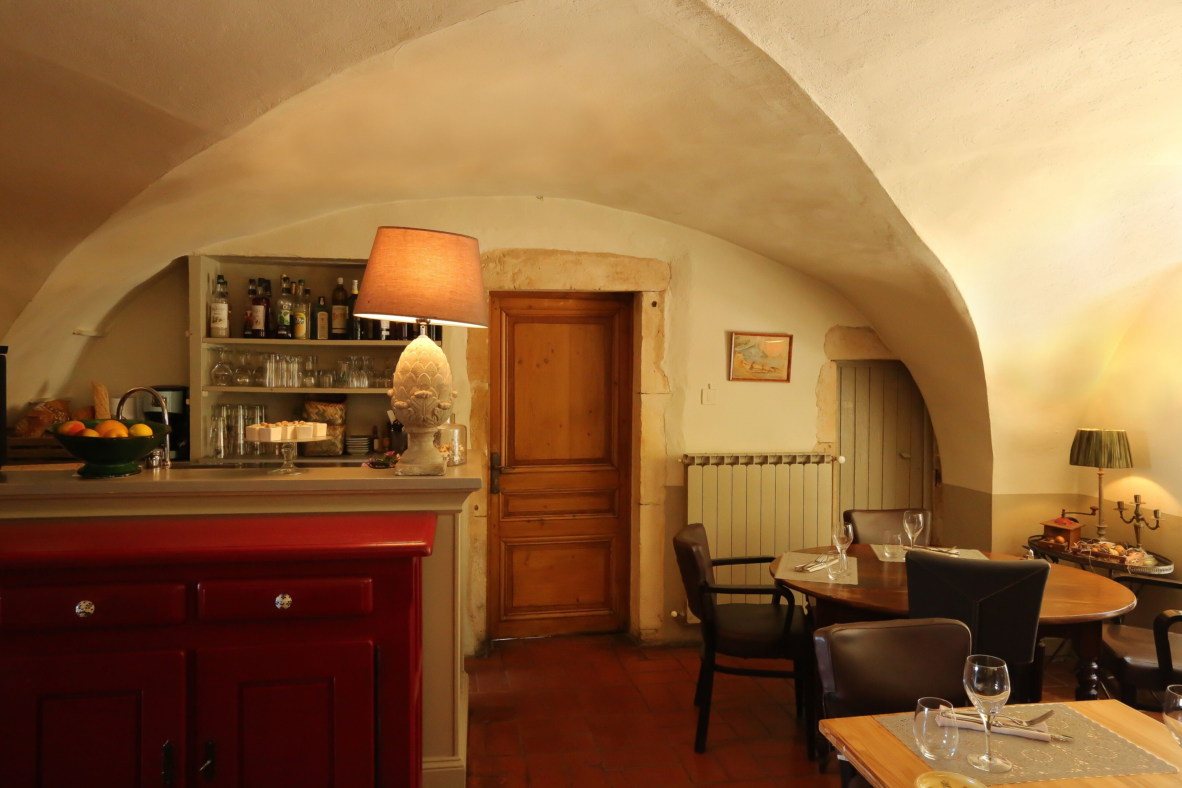 A cozy dining area with a wooden table, chairs, and a bar area with shelves of bottles and glasses.