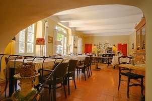 Comedor con mesas y sillas, zona de cocina con armarios y electrodomésticos, y un amplio ventanal que proporciona luz natural.