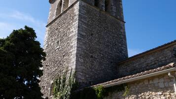 A stone tower with arched windows and a bell, attached to a building with a tiled roof.