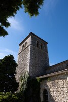 Una torre de piedra con ventanas de arco y una campana, adosada a un edificio con techo de tejas.
