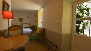Habitación de hotel con cama, una silla, una mesa, una lámpara y ventana con vistas a follaje.