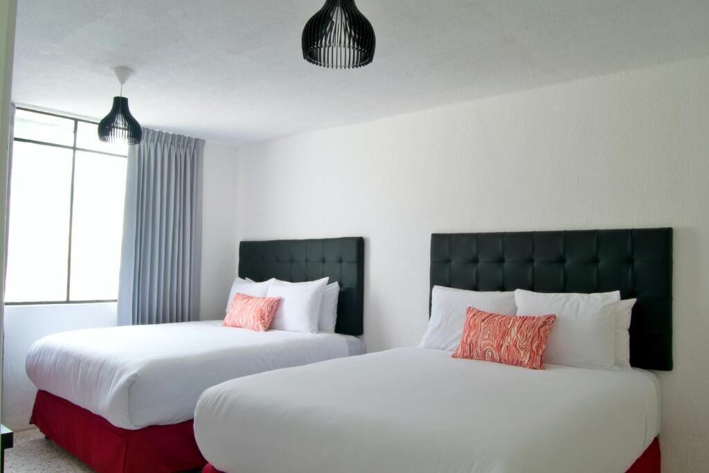 Hotellihuone, jossa on kaksi sänkyä, suuri ikkuna, jossa on verhot, ja musta riippuvalaisin.