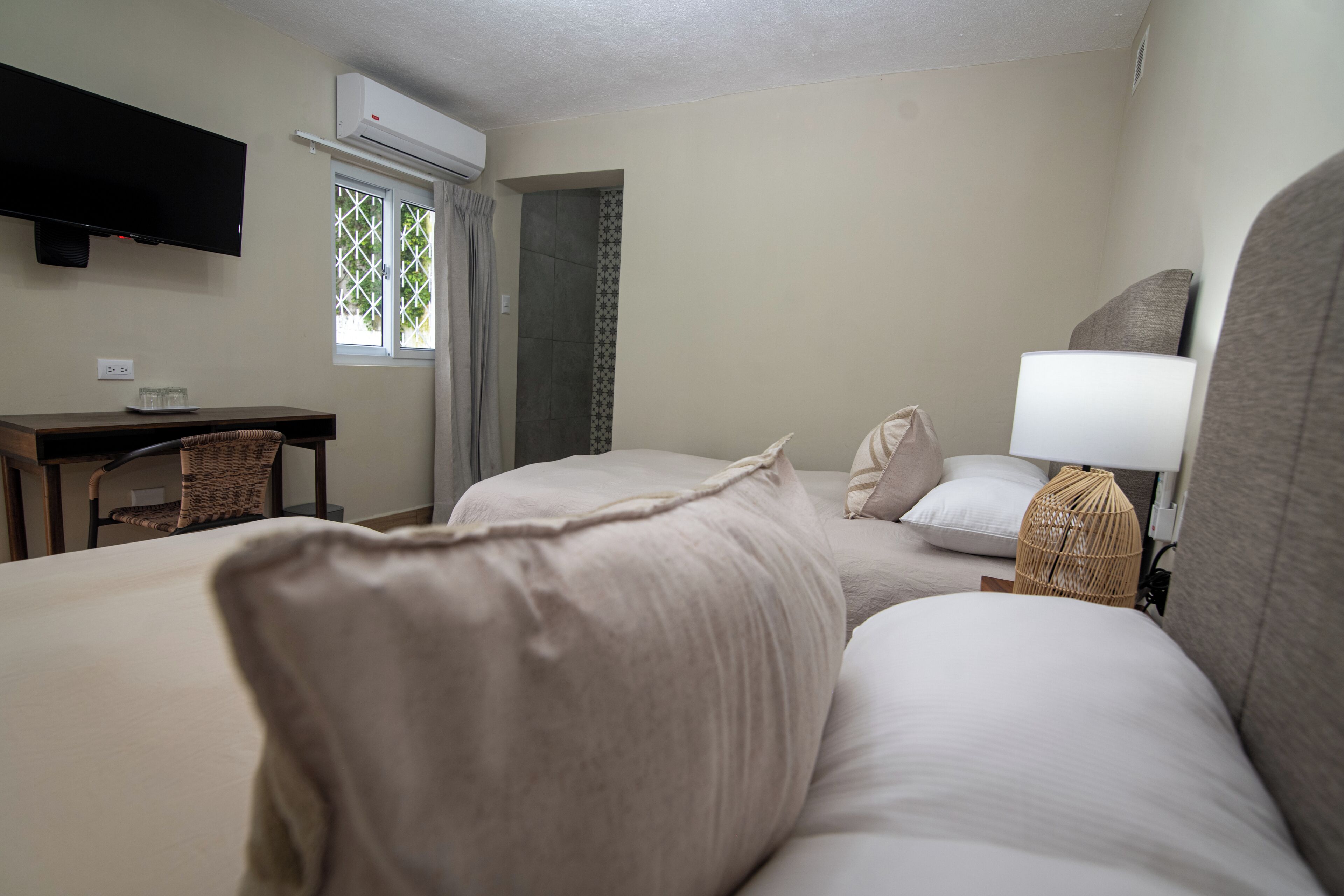 Une chambre d’hôtel avec deux lits, un bureau, une chaise, une télévision et un appareil de climatisation.