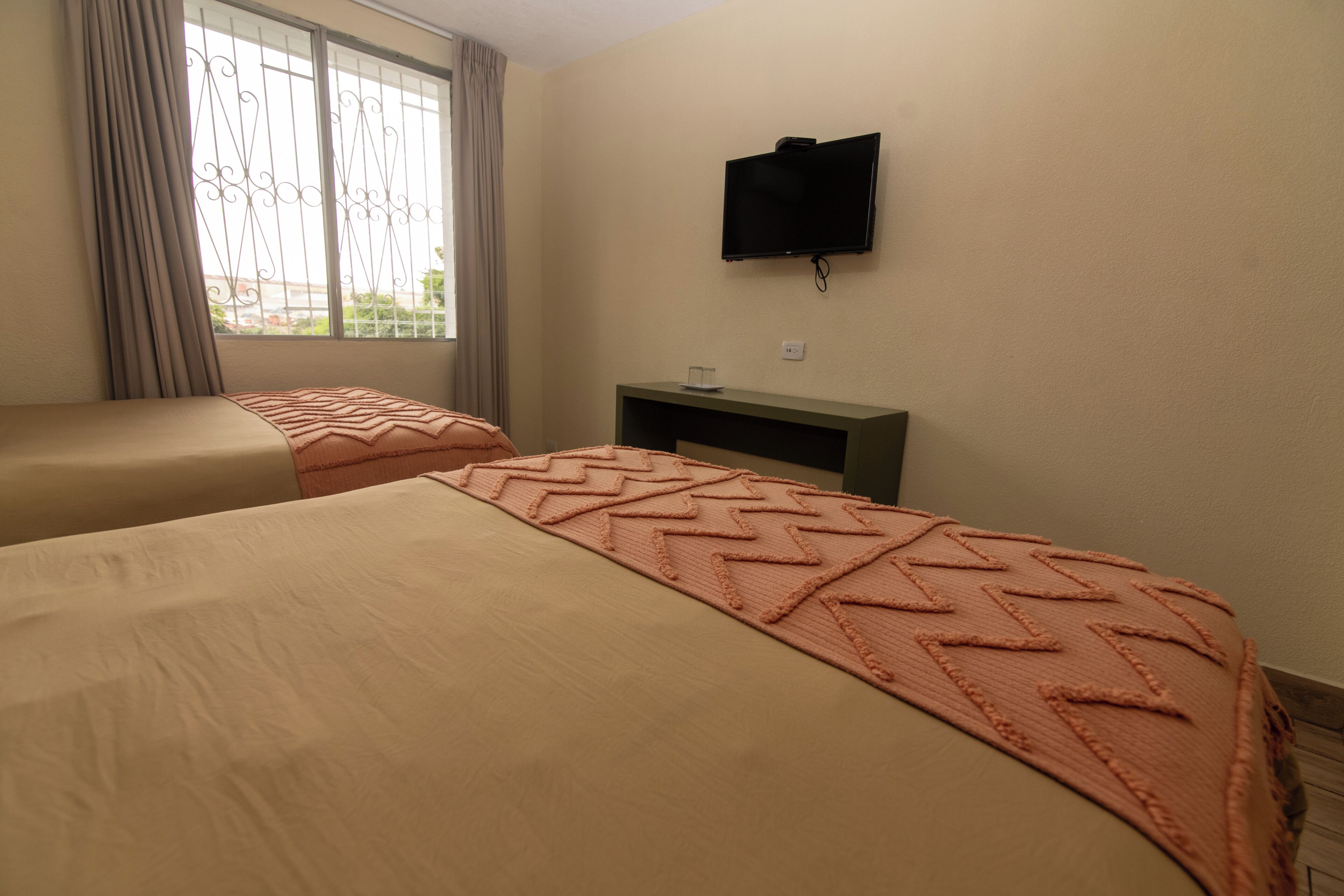 Habitación de hotel con dos camas, un televisor en la pared y una ventana con cortinas.