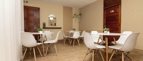 Un comedor con sillas y mesas blancas, piso de madera y una lámpara en el techo.