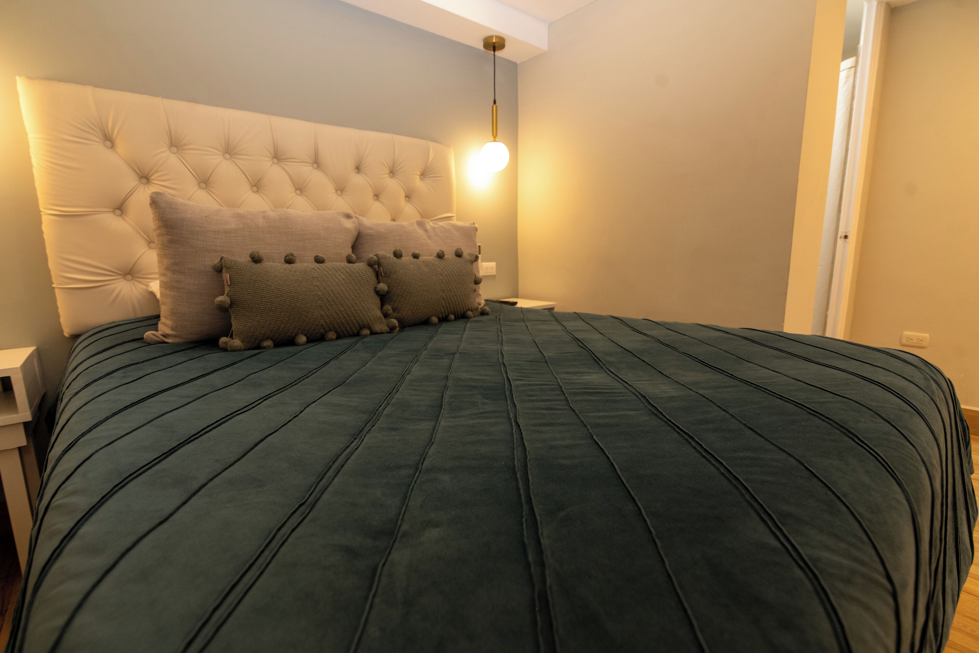 Une chambre à coucher avec une tête de lit capitonnée, une couvre-lit verte et deux oreillers.
