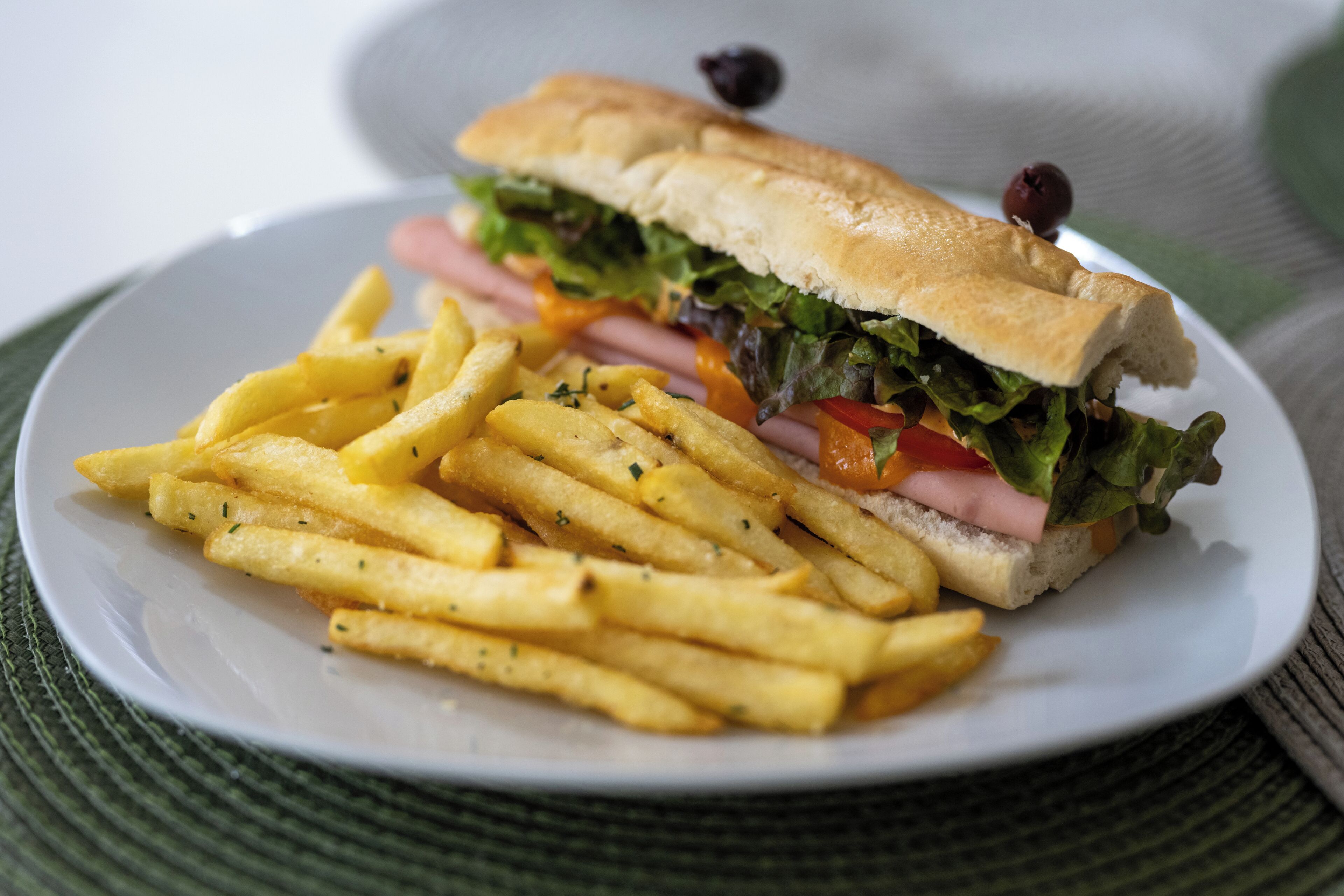 Un sándwich de pan con lechuga, tomate y jamón, acompañado de una porción de papas fritas en un plato blanco.