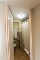 Un baño estrecho con inodoro, cortina de ducha y una toalla colgada en la pared.