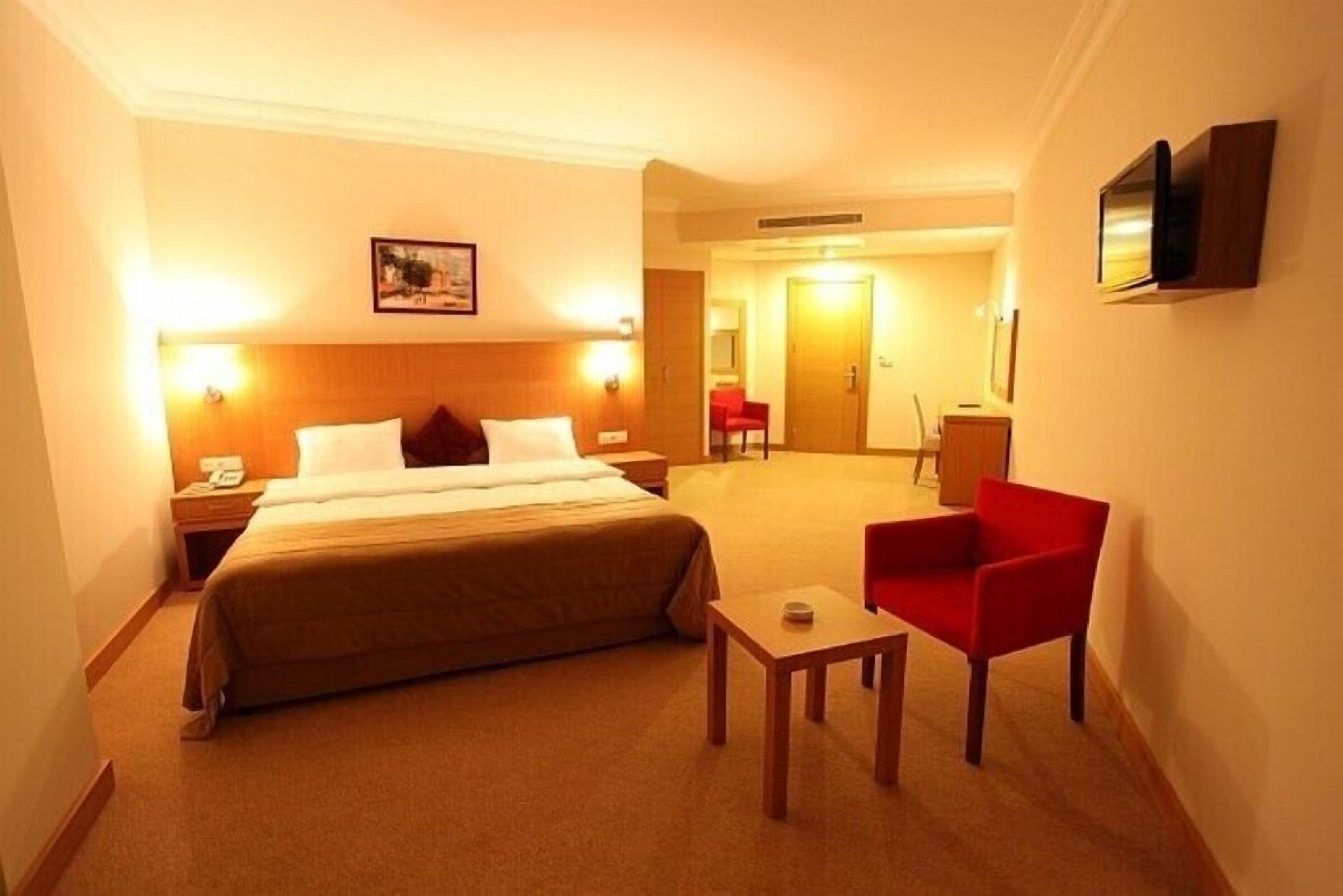 A hotel room with a bed, bedside table, chair, and a television mounted on the wall.