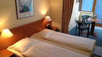 Ein Hotelzimmer mit einem Doppelbett, zwei Nachttischlampen, einem Sessel, einem kleinen Tisch und einem fenster mit Vorhängen.