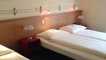 A hotel room with two beds, a nightstand, a lamp, and two wall-mounted paintings.