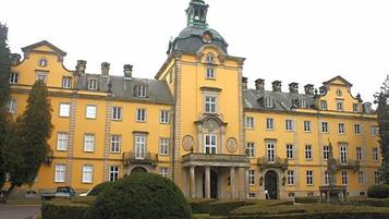 A large yellow building with a central tower, multiple windows, and a well-maintained garden.