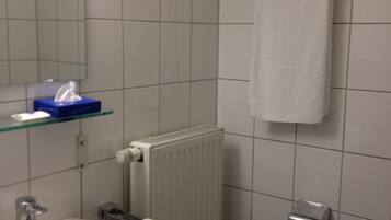 A bathroom with a white sink, a mirror, a towel rack, a radiator, and a toilet paper dispenser.