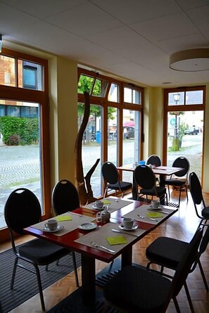 Un área de comedor con mesas y sillas, ventanas amplias y vista a la calle.