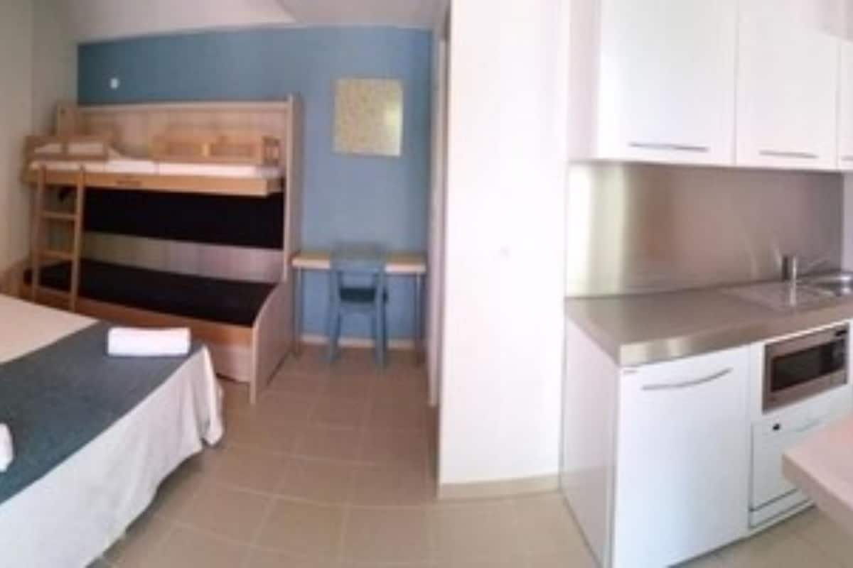 Ein Zimmer mit einem Etagenbett, einem kleinen Schreibtisch und einer Küchenzeile.