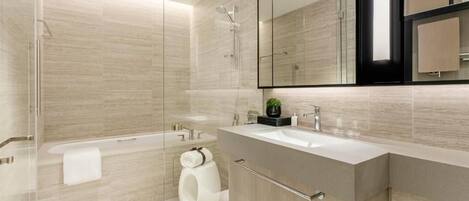A modern bathroom with a glass shower enclosure, a bathtub, and a vanity with a large mirror.