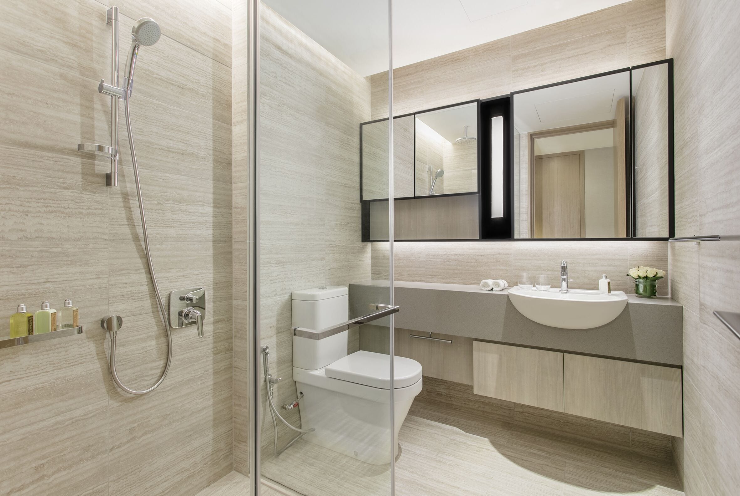 A modern bathroom with a glass shower enclosure, a toilet, a sink, and a large mirror.