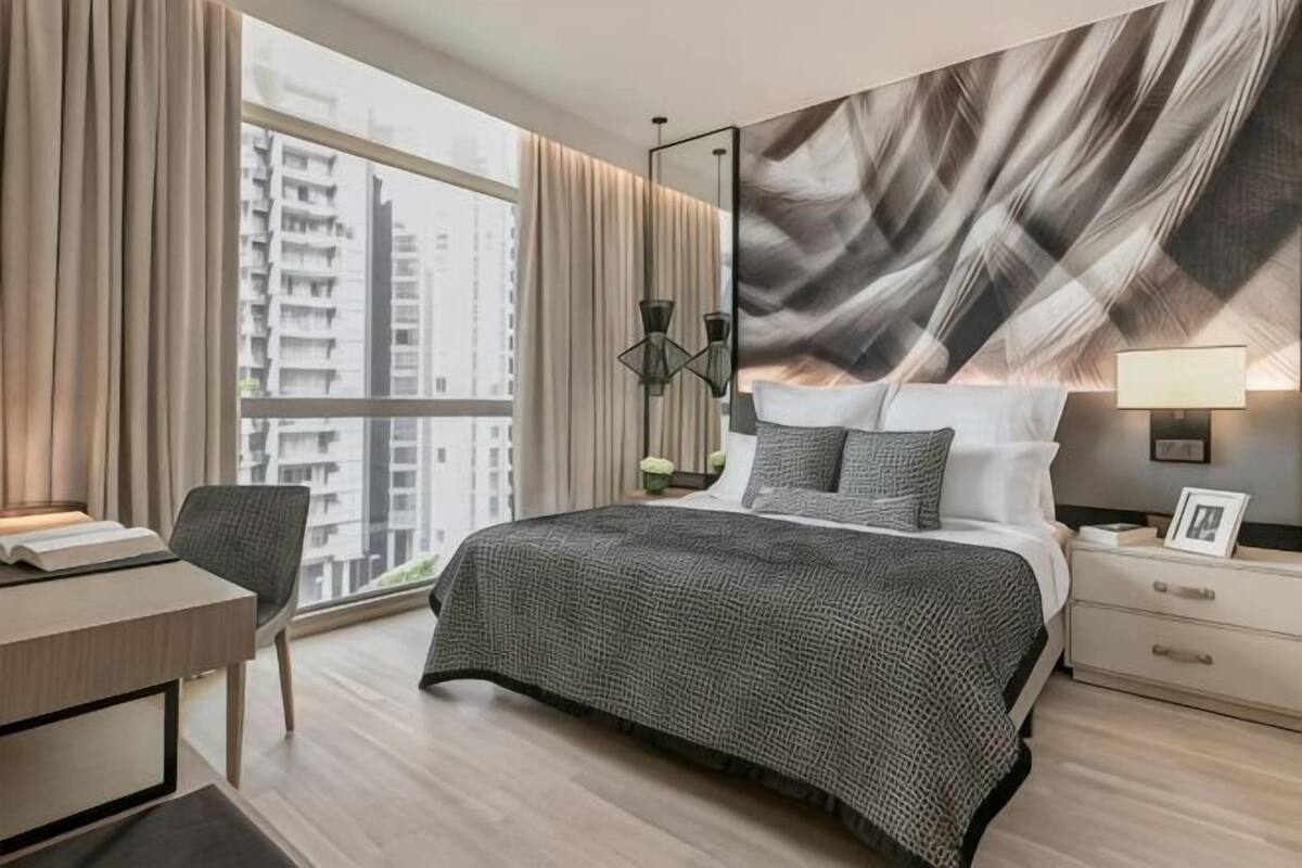 Hotelkamer met een groot bed, een bureau, een stoel, een nachtkastje en uitzicht op gebouwen door een groot raam.