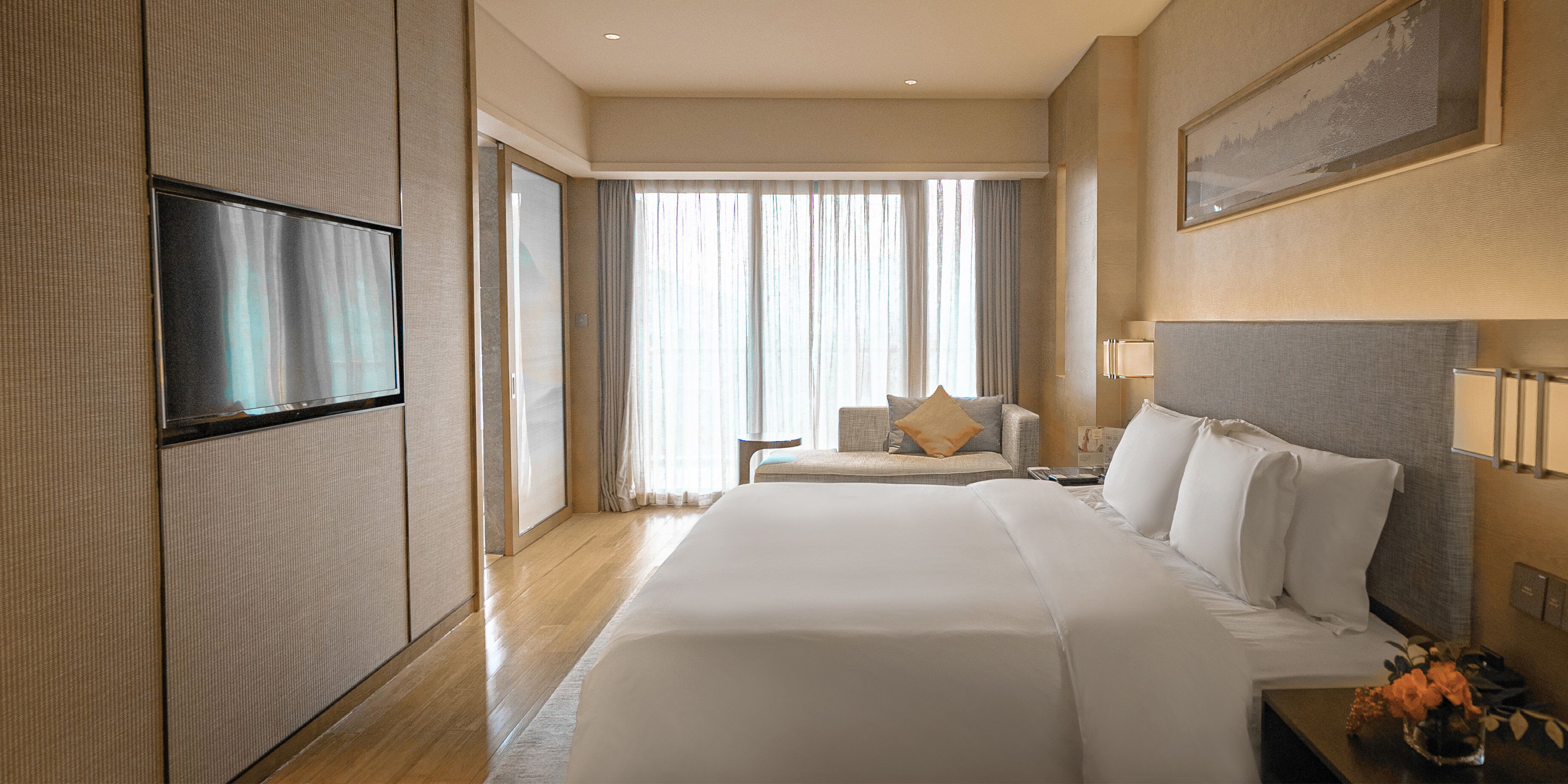 Una camera d'albergo con un letto grande, una televisione a schermo piatto, un divano e una finestra con tende.
