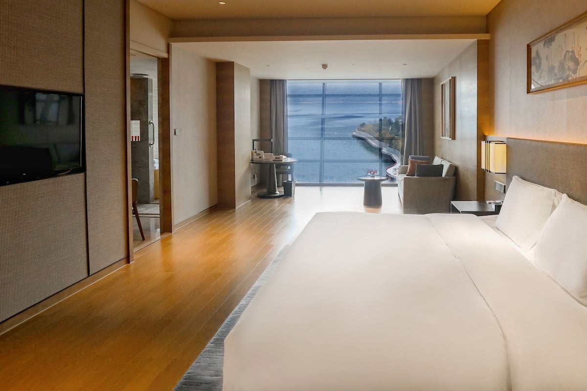 A hotel room with a large bed, a television, a desk, and a view of the sea.