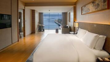 A hotel room with a large bed, a television, a desk, and a view of the sea.