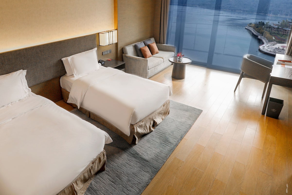 A hotel room with two beds, a sofa, a small table, and a view of a body of water.