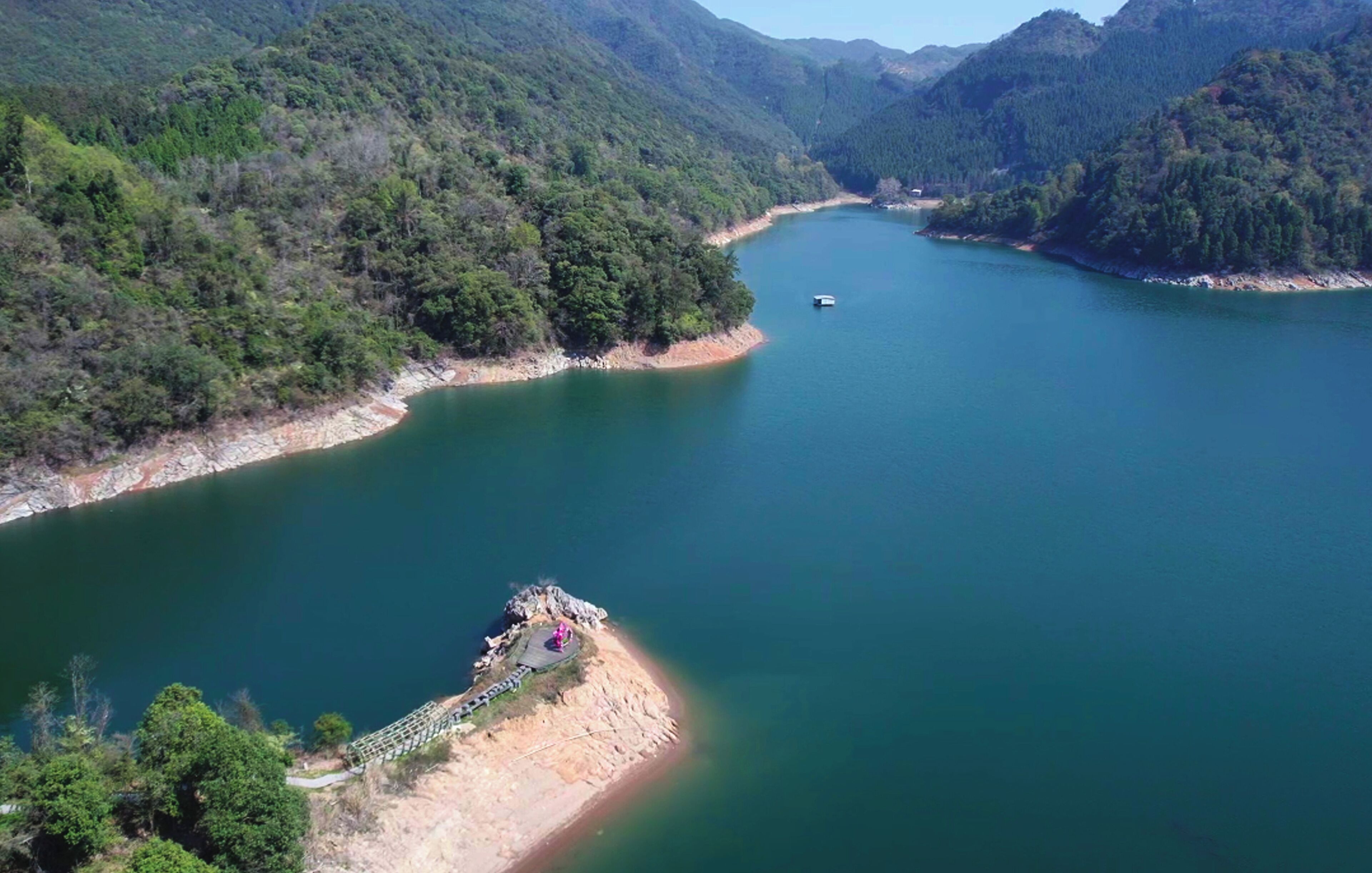 A river surrounded by forested hills with a small dock and a boat.
