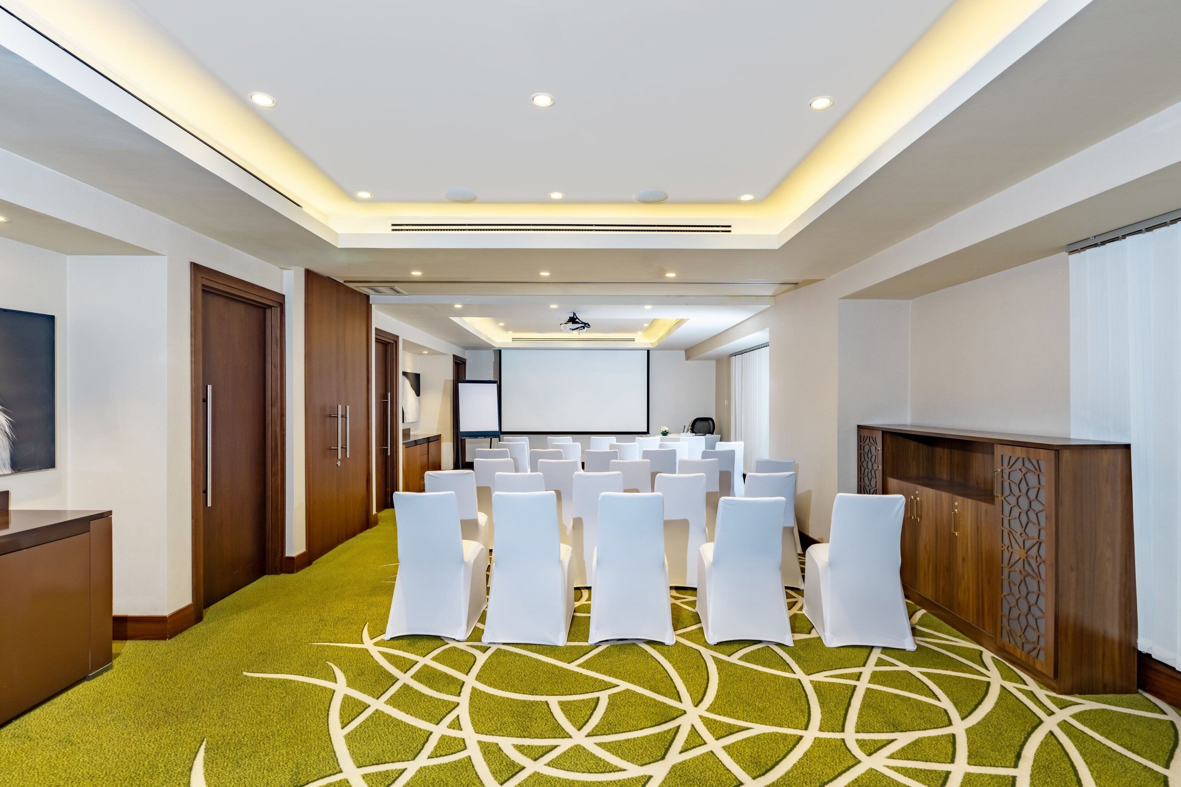 A conference room with rows of white chairs, a projector screen, and a podium.