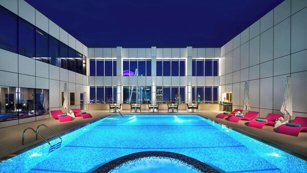 A large indoor swimming pool with a hot tub in the center, surrounded by lounge chairs and tables. - Courtyard by Marriott Riyadh Olaya (Riyadh)