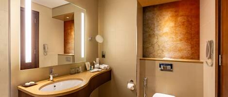 Un baño moderno con un lavamanos curvo, un espejo grande, un inodoro y una zona de ducha.