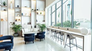 A modern interior with a seating area, a long counter with bar stools, and a large window offering a view of the city. - Courtyard by Marriott Riyadh Olaya (Riyadh)