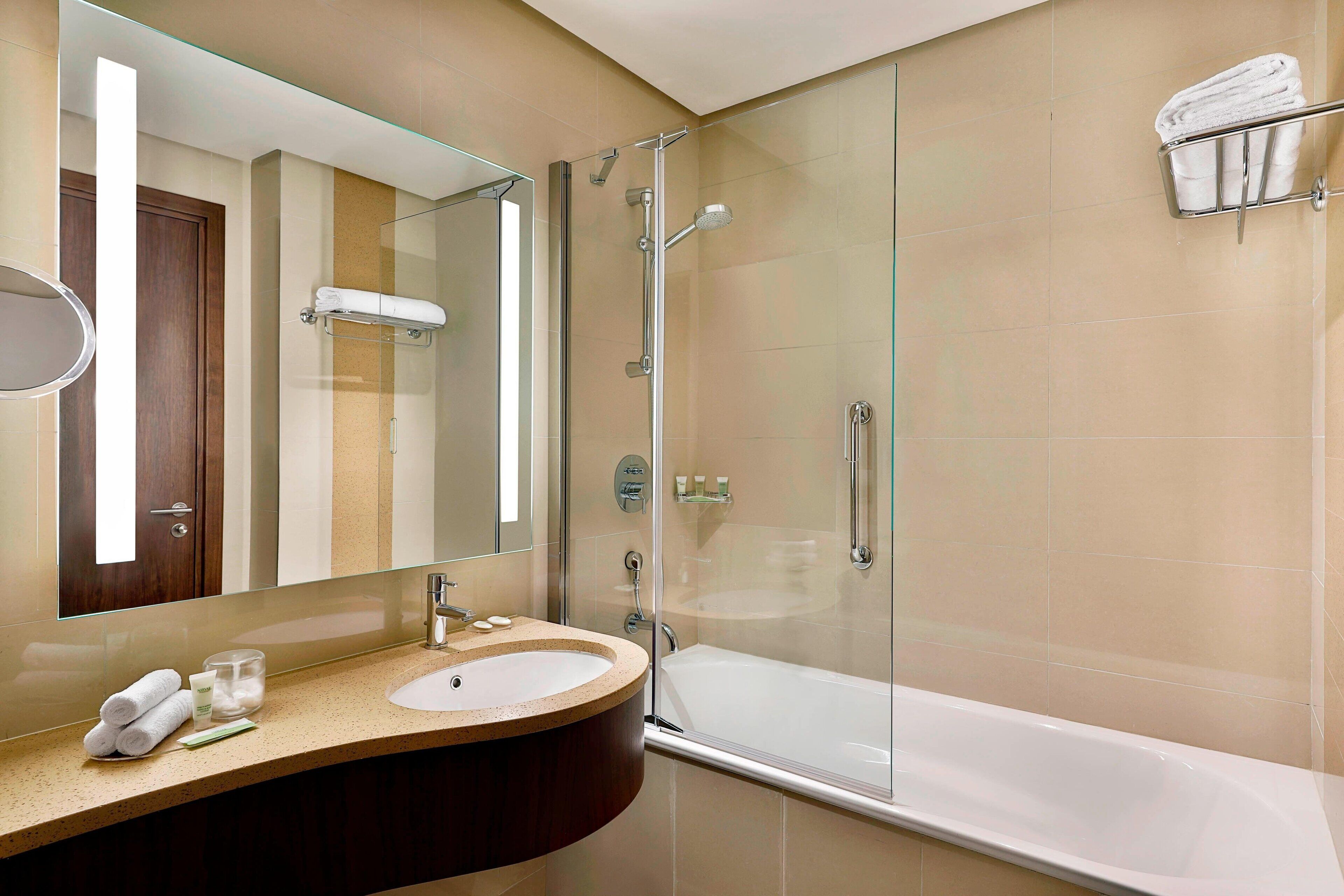 A modern bathroom with a glass shower enclosure, a bathtub, and a vanity with a sink and mirror.