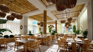 A spacious dining area with natural light, wicker furniture, and hanging baskets. - Courtyard by Marriott Riyadh Olaya (Riyadh)
